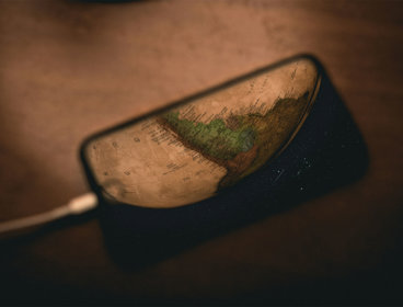 A switched off phone in focus laying on a dark brown, wooden table. An old map is reflected on the phone's screen.