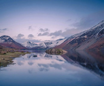 A lake in foreground surrounded by snow-capped mountains.