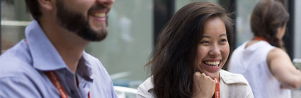 Two people sit next to each other smiling while wearing professional clothing and lanyards.