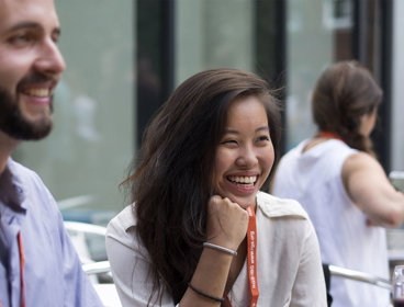 Two people sit next to each other smiling while wearing professional clothing and lanyards.