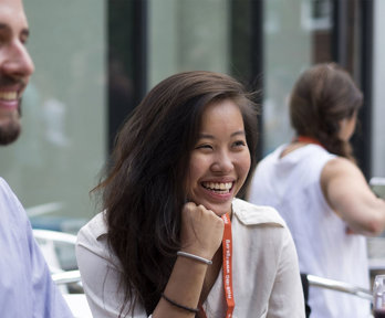 Two people sit next to each other smiling while wearing professional clothing and lanyards.