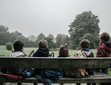 A gorup of children sitting on a bench looking at a field with trees