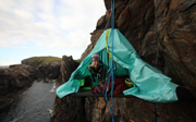 Phoebe Smith on portaledge off the edge of a cliff near water.