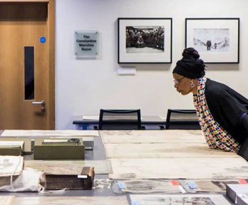 A person looking at historic materials, including maps, books, and photographs spread out on a large table.