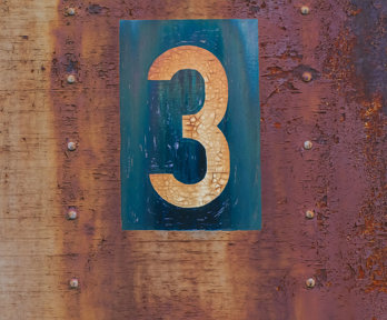 An orange coloured number 3 on a blue background, on a further rusty metal background.