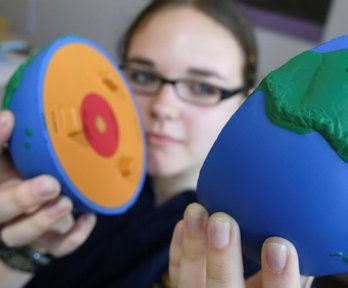 A female student holding a foam globe that has split into two to show what the inside of the earth looks like. The globe shows coloured layers to identify the core of the Earth.