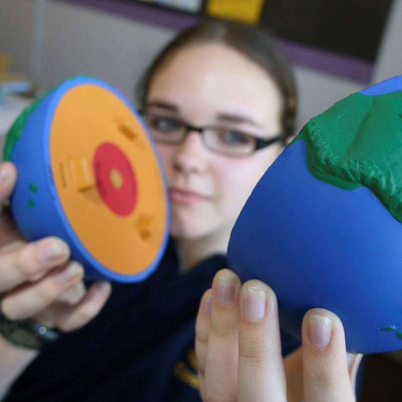 A female student holding a foam globe that has split into two to show what the inside of the earth looks like. The globe shows coloured layers to identify the core of the Earth.