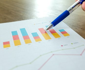 Person holding pen pointing at graphs on piece of paper. 