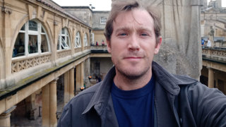 A man taking a picture of himself with Roman baths in the background.