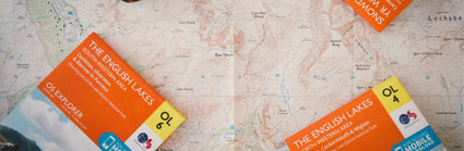 Closed Ordnance Survey maps titled English Lakes laying on top of an open map.