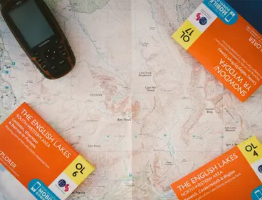 Closed Ordnance Survey maps titled English Lakes laying on top of an open map.