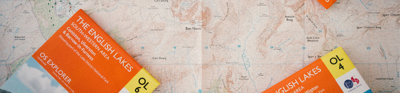 Closed Ordnance Survey maps titled English Lakes laying on top of an open map.