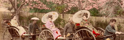 Early 19th century photograph of three geishas on jin rickshaws pulled by three men.