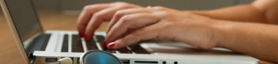 Close-up of a person typing on a laptop. Next to the laptop lays a stethoscope.