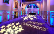 A drinks reception setup with a Merry Christmas projection on the floor of a grand entrance hall.