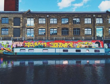 A canal boat with a background of an old industrial building and graffiti