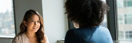 Two people sitting across form each other at a table talking.