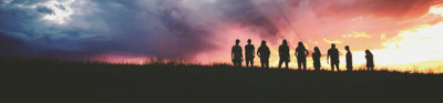 Silhouette of nine people standing on a hill against a sunrise.