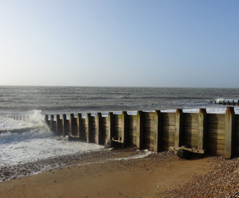 A beach groyne, made of wood, with a sandy and pebbley beach. It's a nice day