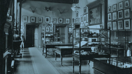 Old black and white photograph of the Geographical Museum showing multiple display cases, paintings on the walls, and a large globe.