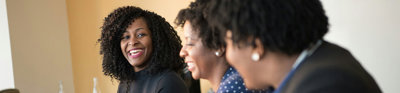 Three people smiling while sitting in a row at a wooden table in an office environment.