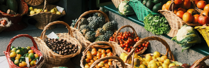 A variety of fruit and vegetables sit in several baskets outside a shop. These include avocado, mango, pineapple, apple, tomato, plum, pear and lemon baskets