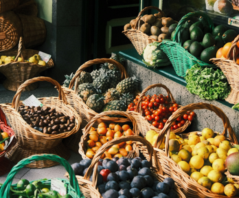 A variety of fruit and vegetables sit in several baskets outside a shop. These include avocado, mango, pineapple, apple, tomato, plum, pear and lemon baskets