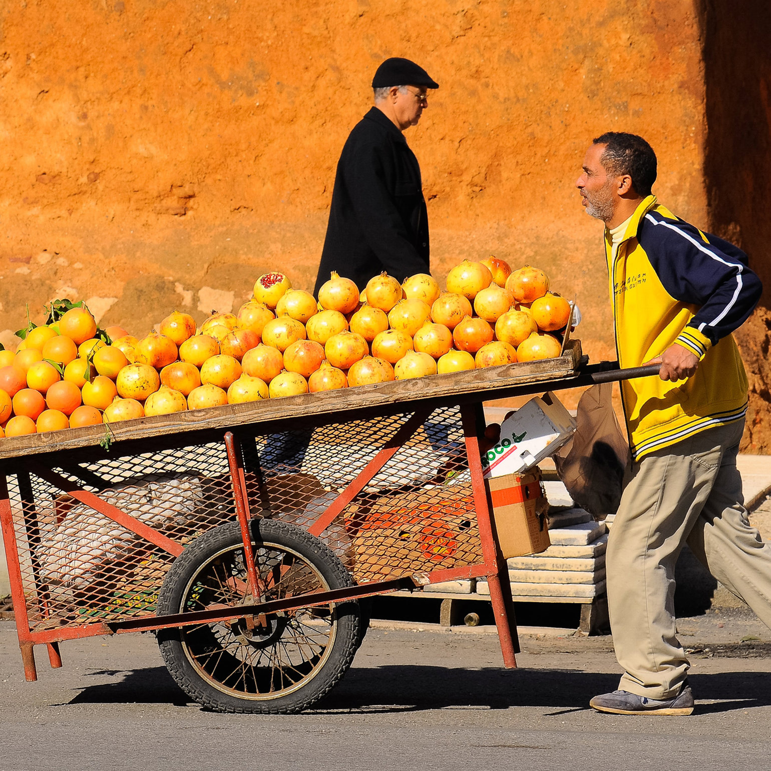 A man pushing a cart loaded with pomegranates