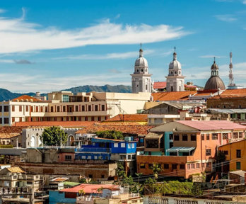 A cluster of buildings of different heights and shapes closely packed together. There are three domed spires and a telecommunications tower that are taller than the other buildings.