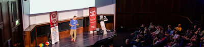 Person presenting next to a poster that says 'CityJS confernce' on a stage in a full theatre lecture hall. 