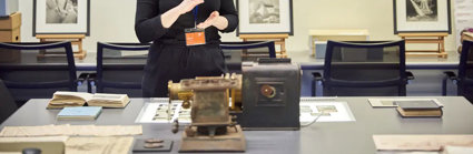 A person standing next to a table with books, glass slides, and scientific instruments on top of it.