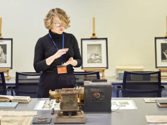 A person standing next to a table with books, glass slides, and scientific instruments on top of it.