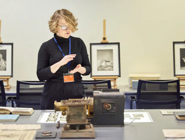 A person standing next to a table with books, glass slides, and scientific instruments on top of it.