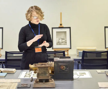 A person standing next to a table with books, glass slides, and scientific instruments on top of it.