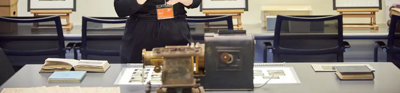 A person standing next to a table with books, glass slides, and scientific instruments on top of it.