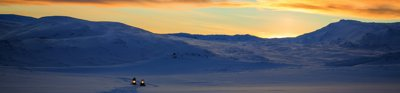 Snow capped mountain with people on snow mobiles and a sunset sky