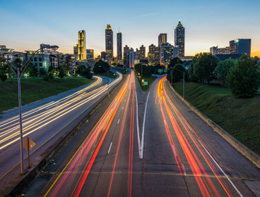 Timelapse of cars on a suburban highway creating light trails leading to a city at golden hour.