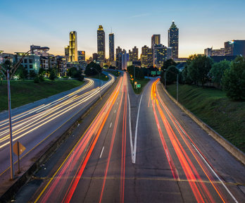 Timelapse of cars on a suburban highway creating light trails leading to a city at golden hour.