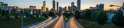 Timelapse of cars on a suburban highway creating light trails leading to a city at golden hour.