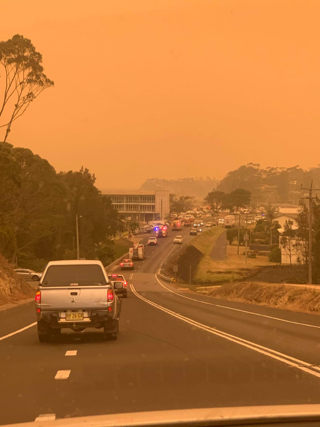 Malua Bay fire fighters are shown rushing to the wildfire. The whole image is orange where the smoke and flames have impacted the colour of daytime