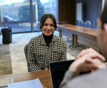 Two people sitting at a desk facing eachother. One is looking at a laptop.