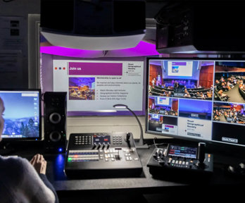 A person sat at a desk working in the recording booth of a lecture theatre.