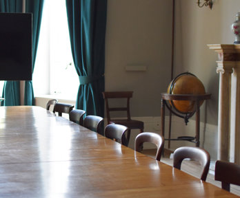 Stately looking meeting room with a large wooden table, tv screen and globe.