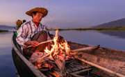 Man on a traditional wooden boat burning a fire.