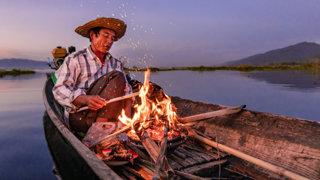 Man on a traditional wooden boat burning a fire.