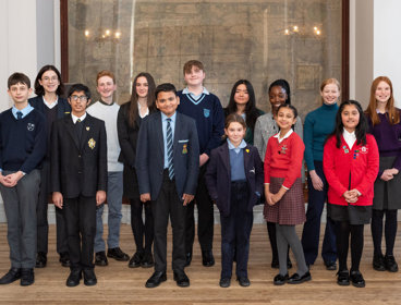 Group of 14 school students standing in front of a large historical map of the world.