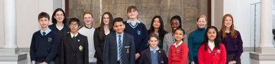 Group of 14 school students standing in front of a large historical map of the world.