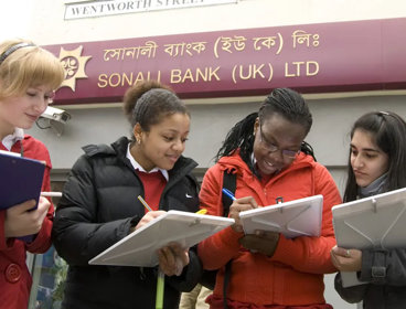 A group of three students with clipboards, collecting information in a high-street area. They are standing outside a bank.