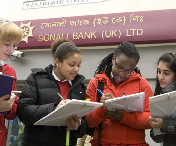 A group of three students with clipboards, collecting information in a high-street area. They are standing outside a bank.