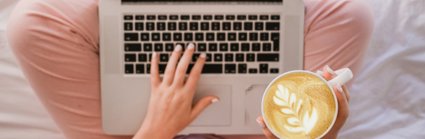 A Laptop on a persons lap with a coffee in their right hand